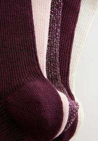 Ribbede sokker i dyb vinrød, blød lyserød og hvid. Det vinrøde par har metalliske tråde. Tekstureret finish med forstærkede tåområder.