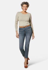 Beige Langarmhemd, kombiniert mit grauen Slim-Fit-Jeans, gesichert mit einem braunen Gürtel und ergänzt durch orangefarbene Absätze. Glatte Texturen, lässiger Stil.