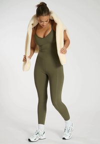 Olivgrön bodysuit med en åtsittande design, ribbad yta och tunna axelband, i kombination med en krämfärgad fleecejacka och atletiska sneakers.