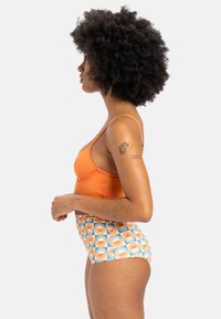 Bikini de talle alto con top naranja y braguita con estampado de diseños geométricos de ráfagas de sol en naranja y turquesa sobre fondo blanco.