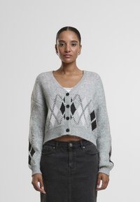 Siva skrajšana cardigan z črno-belo diamantno vzorcem, z globokim V-izrezom in petimi sprednjimi gumbi. Pletena tekstura, dolgi rokavi.