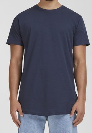 Man wearing a plain navy blue short-sleeve t-shirt and light blue jeans, standing with arms relaxed by sides.