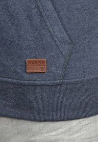Dunkelblaues Sweatshirt mit geripptem Saum und einem braunen Lederetikett, auf dem der Text "BLEND GLOBAL JEANMAKERS" aufgestickt ist.