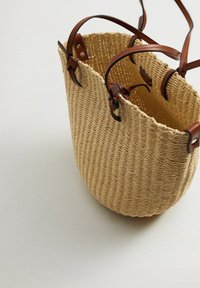 Sac seau en paille tissée avec des anses en cuir, présentant une forme arrondie, une couleur beige naturelle et un motif texturé.