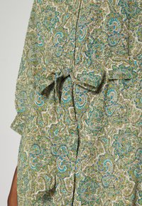 Vihreä ja sininen paisley-kuvioinen kangas, jossa on teksturoitu pinta, ja joka sisältää solmukkeen vyötäröllä sekä napit edessä.