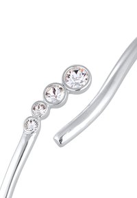 Silverfärgad armband med fyra klara rund kristaller i olika storlekar, med en elegant, böljande design och slät yta.