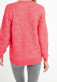 Maglione rosa lavorato a maglia con un motivo circolare testurizzato, polsini e orlo a costine, e una vestibilità rilassata. Indossato con jeans fitted grigi.