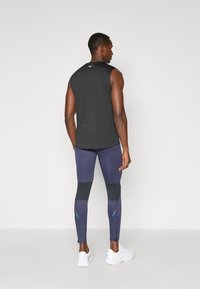 Top deportivo negro sin mangas, leggings azul oscuro con paneles de malla, cremalleras de contraste y zapatillas blancas. Vista trasera mostrada.