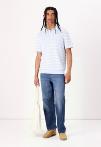 Lyseblå kortærmet polo med stripe mønster og ribbede kanter, parret med blå jeans og beige sneakers. Holder en beige tote bag.
