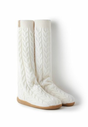 Białe, dziergane skarpetki za kolano z warkoczowym wzorem, ściągaczami i beżową gumową podeszwą zapewniającą przyczepność i trwałość.