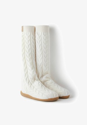 Chaussettes montantes en tricot blanc avec un motif torsadé, des bords côtes et une semelle en caoutchouc beige pour l'adhérence et la durabilité.