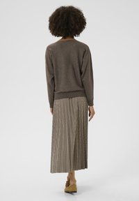 Brūns adīts džemperis ar ribotu apakšmalu apvienots ar garu, šķērssvītrainu svārku ar krokām. Modelis valkā brūnas zamšādas kurpes.