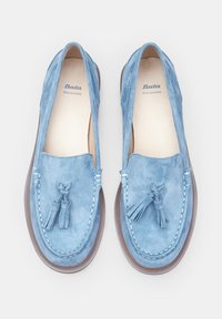 Zilā zamša loafers ar vizuļiem, dabiskā ādas iekšpuse un kontrastējošs brūns gumijas ārējais zole. Atvērtās malas uzlabo elpojamību.