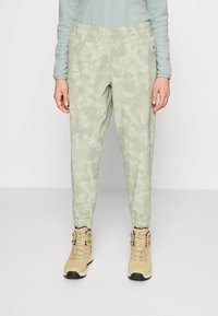 Ljusgröna camouflage-mönstrade joggers med elastisk midja, tapered ankle och sidofickor, kombinerat med beige höga stövlar.