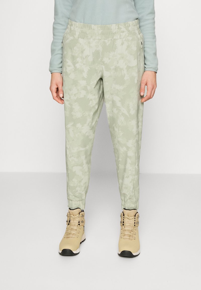 Ljusgröna camouflage-mönstrade joggers med elastisk midja, tapered ankle och sidofickor, kombinerat med beige höga stövlar.