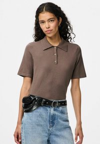Brown short-sleeve polo shirt with a collar, featuring buttons down the front. Paired with high-waisted denim and a black belt bag.