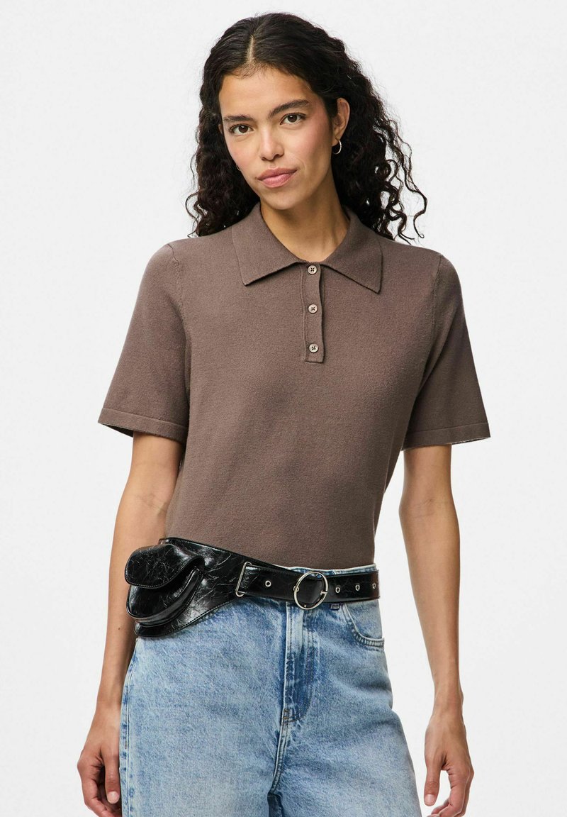 Brown short-sleeve polo shirt with a collar, featuring buttons down the front. Paired with high-waisted denim and a black belt bag.