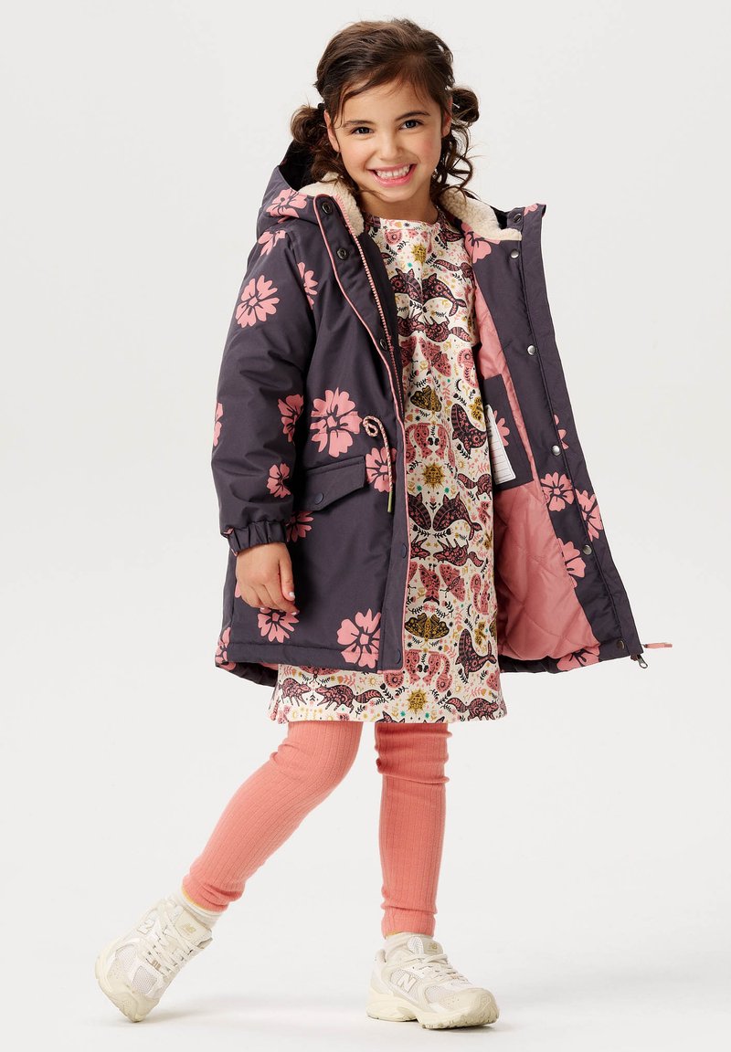 Flickors blommönstrade parka i mörk marinblå med rosa blommor, fodrad med mjuk rosa. Kombinerad med en dekorativ klänning och rosa ribbade leggings.