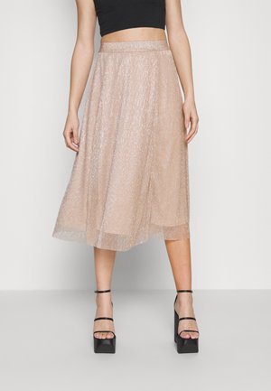 Vrouw die een roségouden metallic midi-rok draagt met een hoge taille, gecombineerd met zwarte platformsandalen met hakken en een zwart cropped topje.