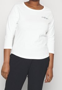 Witte langemouwen T-shirt met een ronde halslijn en geborduurd "Hilfiger" logo op de linkerkant van de borst. Gemaakt van zachte, lichte stof.