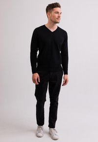Maglione nero a scollo a V in tessuto morbido, abbinato a pantaloni neri e sneakers bianche. Design semplice, vestibilità aderente, senza motivi o dettagli visibili.