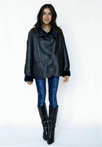 Sort oversized læderjakke med knaplukninger og blå pelsforet krave, kombineret med skinnende blå fløjlstights og høje sorte støvler med hæl.