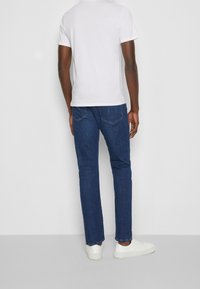 Donkerblauwe spijkerbroeken met rechte pijpen, subtiele contraststiksels en achterzakken. Gecombineerd met witte lage schoenen en een eenvoudig wit T-shirt.