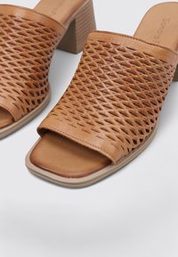 Mules de tacón de cuero tejido en tono marrón con punta abierta. Presentan un empeine estampado y un tacón en bloque beige para mayor soporte y estabilidad.