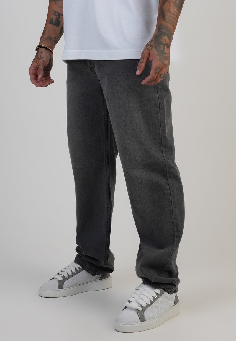 Dunkelgraue Jeans aus Denim mit einer lockeren Passform, kombiniert mit weißen Sneakers mit grauen Akzenten und einem strukturierten Design an den Seiten.