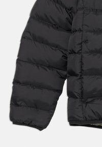Manche de doudoune noire avec des sections matelassées horizontales, texture lisse, poignet élastique et un motif intérieur caché.