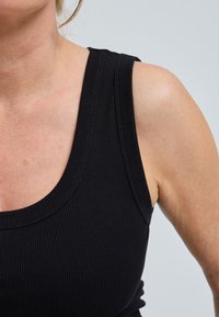 Zwarte geribde tanktop met een ronde hals en brede schouderbanden, met een gladde textuur en een aansluitend ontwerp. Huid zichtbaar op de schouder.