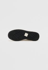 Semelle de basket en caoutchouc noir avec des motifs de bande de roulement texturés et un accent rectangulaire. Partie supérieure de couleur claire visible le long des bords.