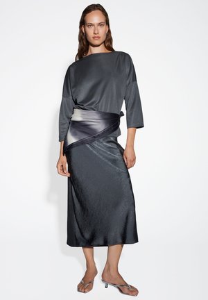 Top grigio scuro, simile a raso, con una vestibilità ampia e maniche a tre quarti, abbinato a una gonna lunga texturizzata con una fascia in gradiente scuro.