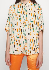 Short-sleeve button-up shirt in cream fabric featuring an abstract pattern in orange, green, and black. Lightweight with a relaxed fit.