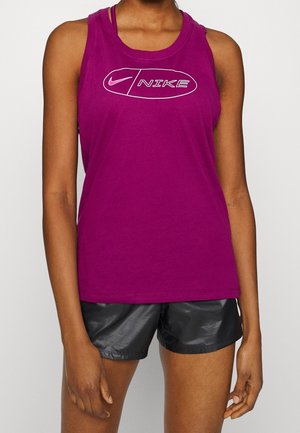 Femme portant un débardeur violet Nike sans manches et un short de sport noir brillant, debout devant un fond uni.