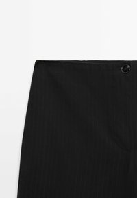 Jupe noire taille haute avec fines rayures, poche latérale et fermeture par un seul bouton noir à la taille.