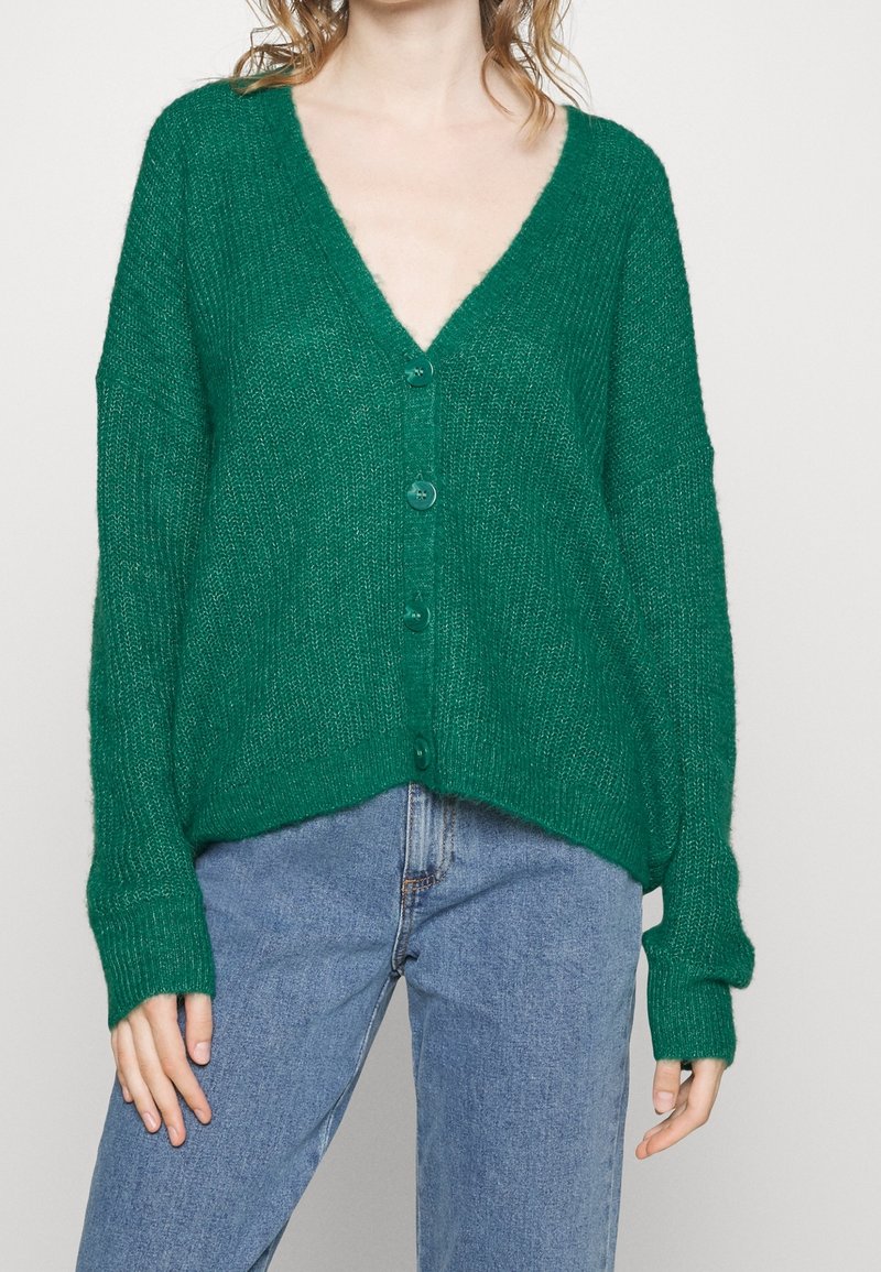 Cardigan vert en maille avec col en V, fermeture à boutons et manches amples, doté d'une finition texturée et d'une coupe décontractée.
