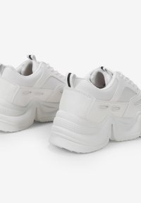 Zapatillas blancas y gruesas con parte superior de cuero suave, suela de goma texturizada y sutiles acentos negros en el talón y la lengüeta.