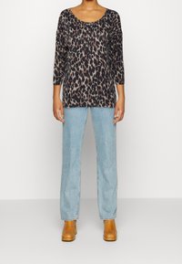 Topp med leopardmönster och trekvartsärmar, rundad halsringning och avslappnad passform, kombinerad med ljusblå högmidjade jeans och bruna ankelstövlar.