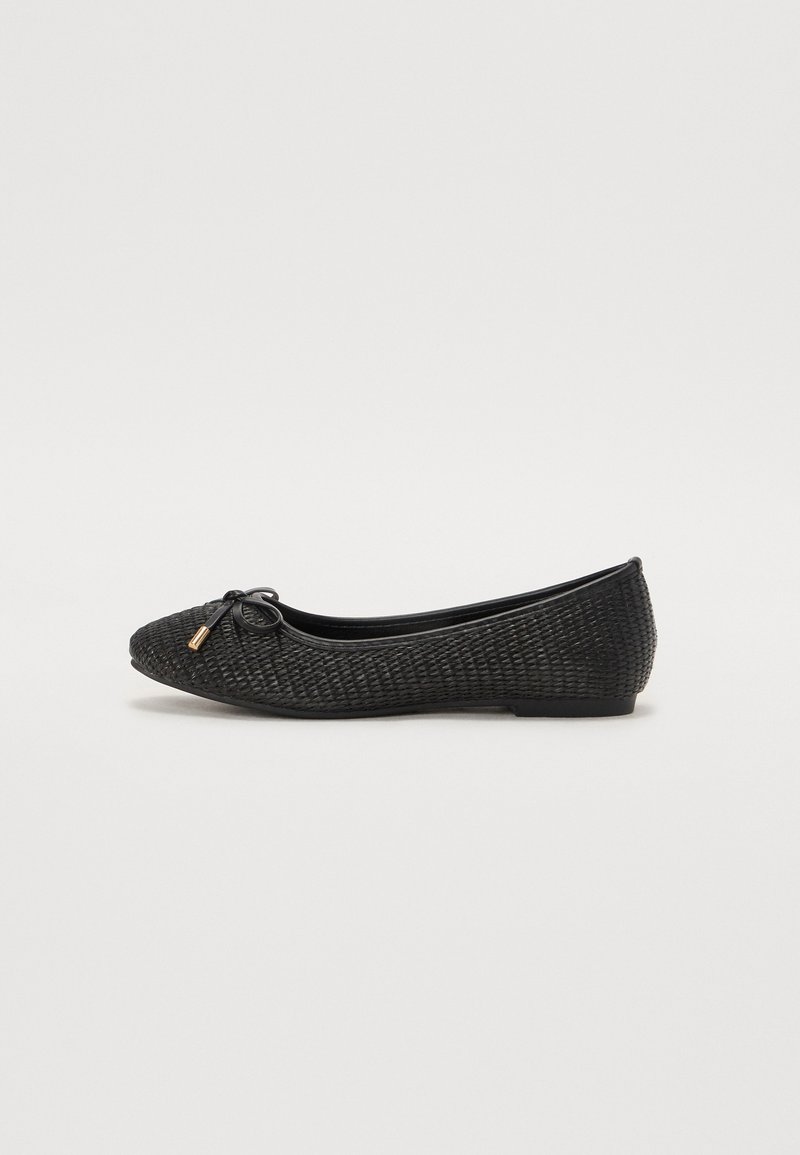 Chaussure plate de ballet noire tissée avec bout arrondi, petit nœud avec embouts dorés et semelle plate sur fond blanc uni.