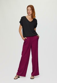 Zwart top met korte mouwen en V-hals, gecombineerd met wijde, magentakleurige broeken. De broeken hebben zijzakken en een relaxed fit. Zwarte sandalen met bandjes.
