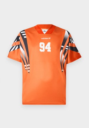 Oranžový športový dres s krátkymi čiernymi a bielymi vzorovanými rukávmi. Na prednej strane má bielu potlač čísla "94" a na hrudi logo Adidas.