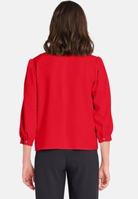Blusa rossa con maniche a tre quarti e vestibilità comoda. Tessuto liscio, pieghe sottili sulle spalle e polsini con bottoni. Vista posteriore mostrata.