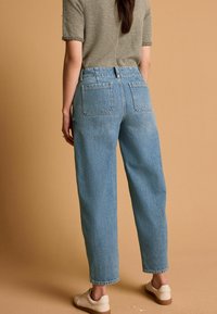 Jeans a vita alta di colore blu chiaro con una vestibilità rilassata, dotati di due tasche posteriori, orli sfrangiati e abbinati a sneakers beige chiaro.