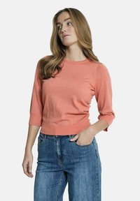 Koraalrode sweater met een ronde halslijn en driekwartmouwen. Gemaakt van een zachte, gestructureerde stof. Gecombineerd met high-waisted denim jeans.