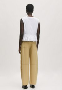 Witte mouwloze top met een gerimpelde zoom, gecombineerd met beige wijde cargo-broek met grote zakken. Gladde stoftextuur, casual pasvorm.