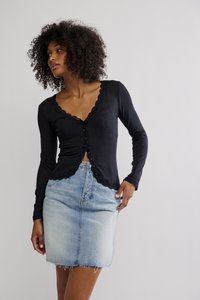 Crna majica s dugim rukavima s čipkastim rubom i kopčanjem na gumbe, uparena s traper suknjom svijetloplave boje s izgužvanim rubom.