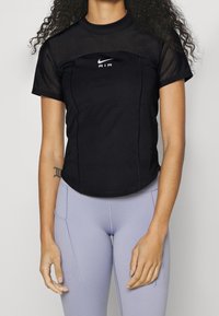 Camiseta deportiva negra de manga corta, con paneles de malla y un logo blanco de Nike Air en el pecho, combinada con leggings lilas claros.