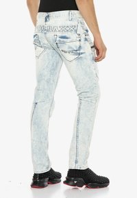 Hellblau gewaschene Jeans im Slim-Fit-Stil mit hoher Taille, kontrastierenden Nähten und mehreren Gesäßtaschen. Logo auf dem Bund sichtbar.