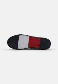Suola di scarpa in gomma nera con un design di skyline in sezioni grigie, bianche e rosse, con "TOMMY HILFIGER" impresso nell'area rossa.